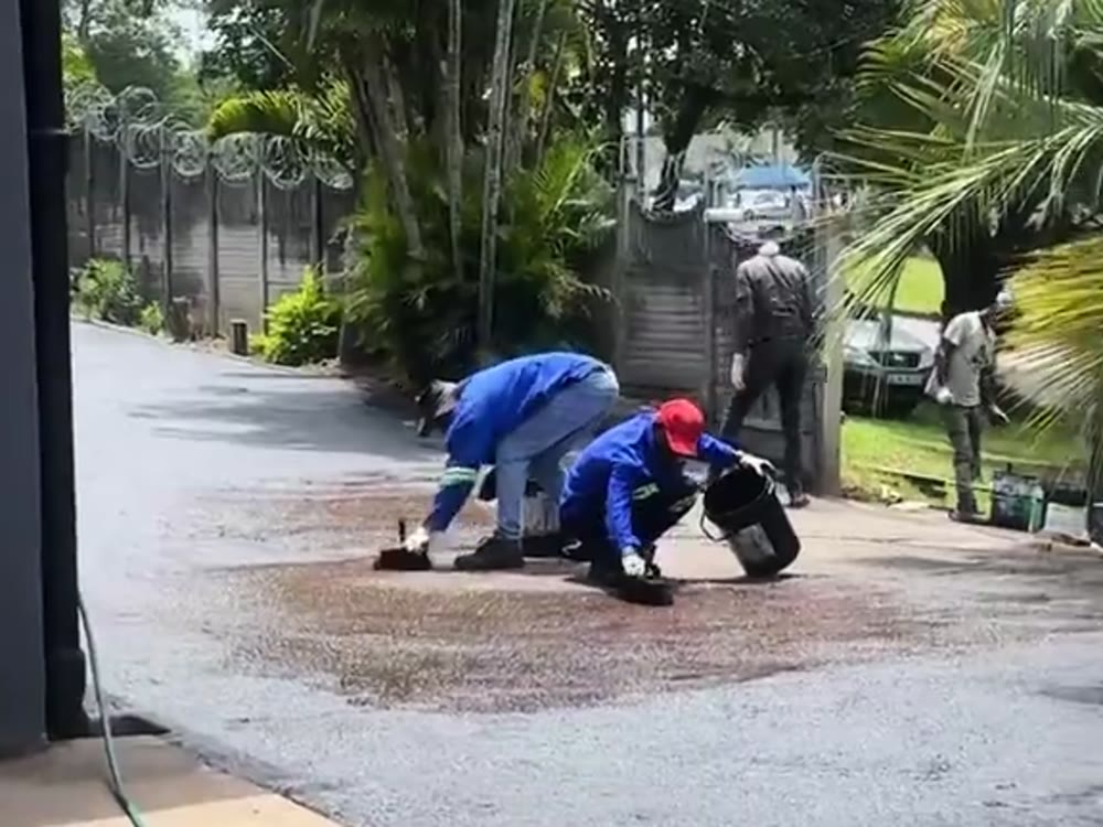 Worker hand-finishing a wet asphalt patch by the front steps