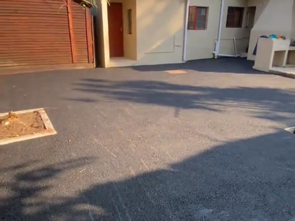 Home driveway finished in dark asphalt beside a stone retaining wall