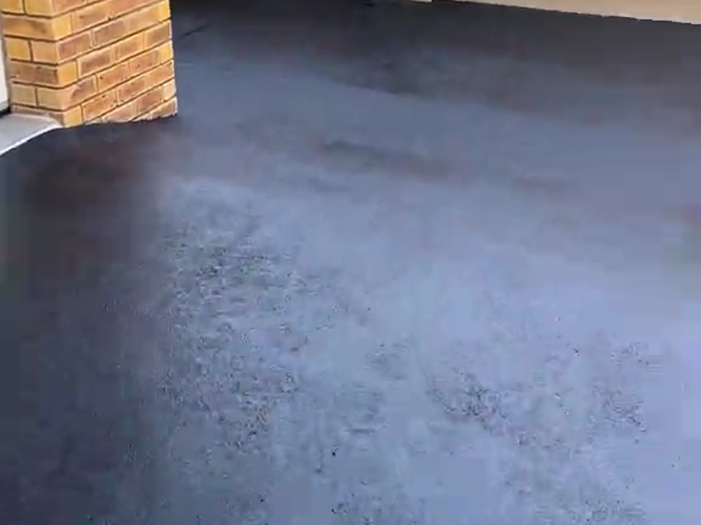 Freshly laid black asphalt driveway alongside a brick boundary wall